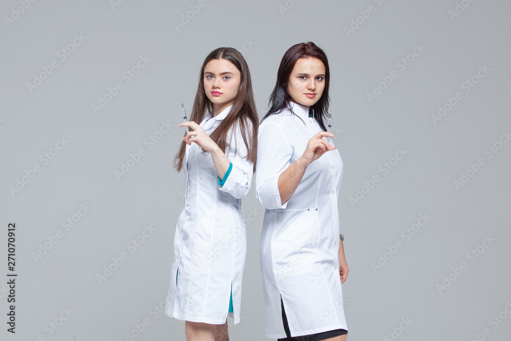 Two female doctors standing back-to-back hold ready-to-inject syringes