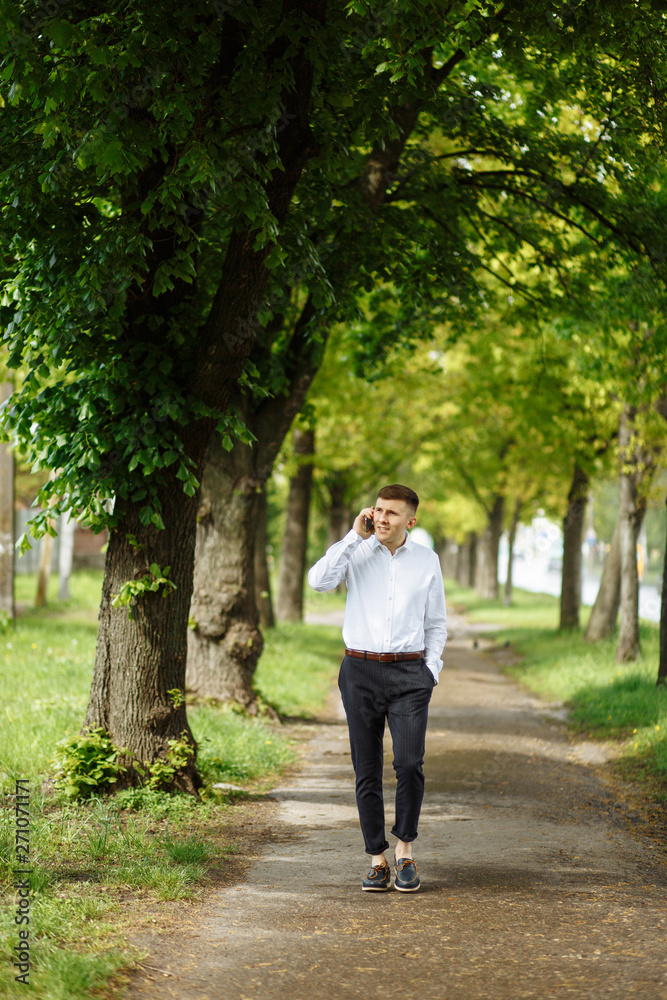 Young man talking on his phone while walking in the park Young man talking on his phone while walking in the park