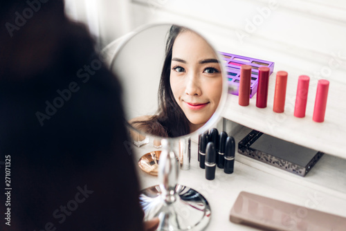 Smiling young beautiful asian woman fresh healthy skin looking on mirror with makeup cosmetics set at home.facial beauty and cosmetic concept