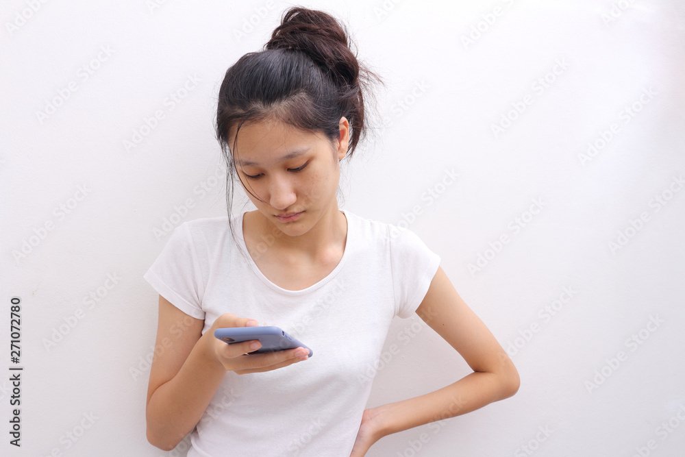 Beautiful young Asia woman  , Satisfied lovely woman holds modern cell phone, texts with friend online in chat, against white wall, connected to high speed internet. Shot of teenager with device