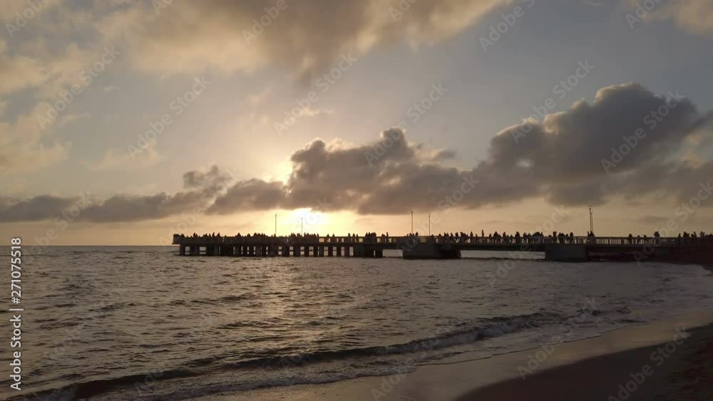 Beautiful golden sunset in the Roman coast at Ostia Lido with light reflections on the sea water and the people silhouette on the pier Beautiful golden sunset in the Roman coast at Ostia Lido with light reflections on the sea water and the people silhouette on the pier