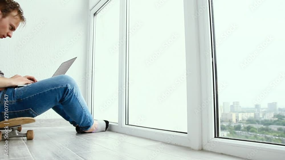 young male programmer working with a laptop on a balcony overlooking the city, sitting on a skateboard young male programmer working with a laptop on a balcony overlooking the city, sitting on a skateboard