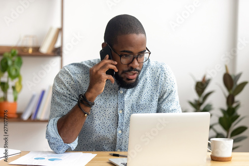Serious african-american employee making business call focused on laptop screen photo