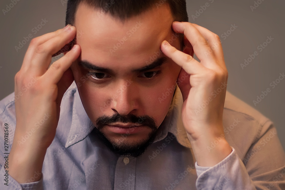 Closeup portrait of a stressed middle-aged man in grey shirt sitting indoor with sad face and thinking holding head in hands. Financial crisis, job problems, health issues concept