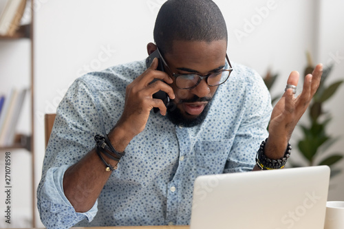 Angry mad african-american businessman talking on cellphone in office