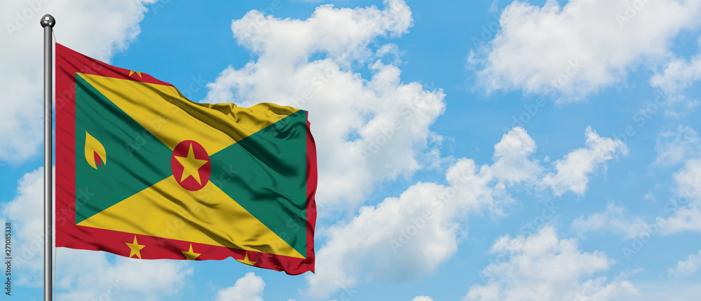 Grenada flag waving in the wind against white cloudy blue sky. Diplomacy concept, international relations.