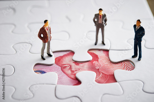 Miniature men with Chinese currency in jigsaw puzzle 