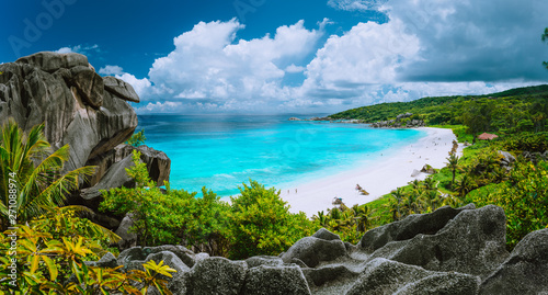 Picturesque panoramic shot of Grand Anse, La Digue island, Seychelles. Huge granite rock formation, bright white sand tropical beach with turquoise blue crystal clean water and cloudscape