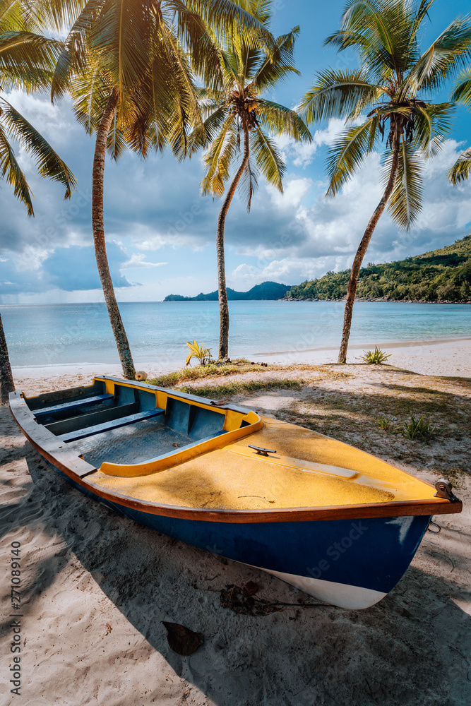 Boat under coconut palm trees on sunny day on shore of tropical beach, Seychelles islands Boat under coconut palm trees on sunny day on shore of tropical beach, Seychelles islands