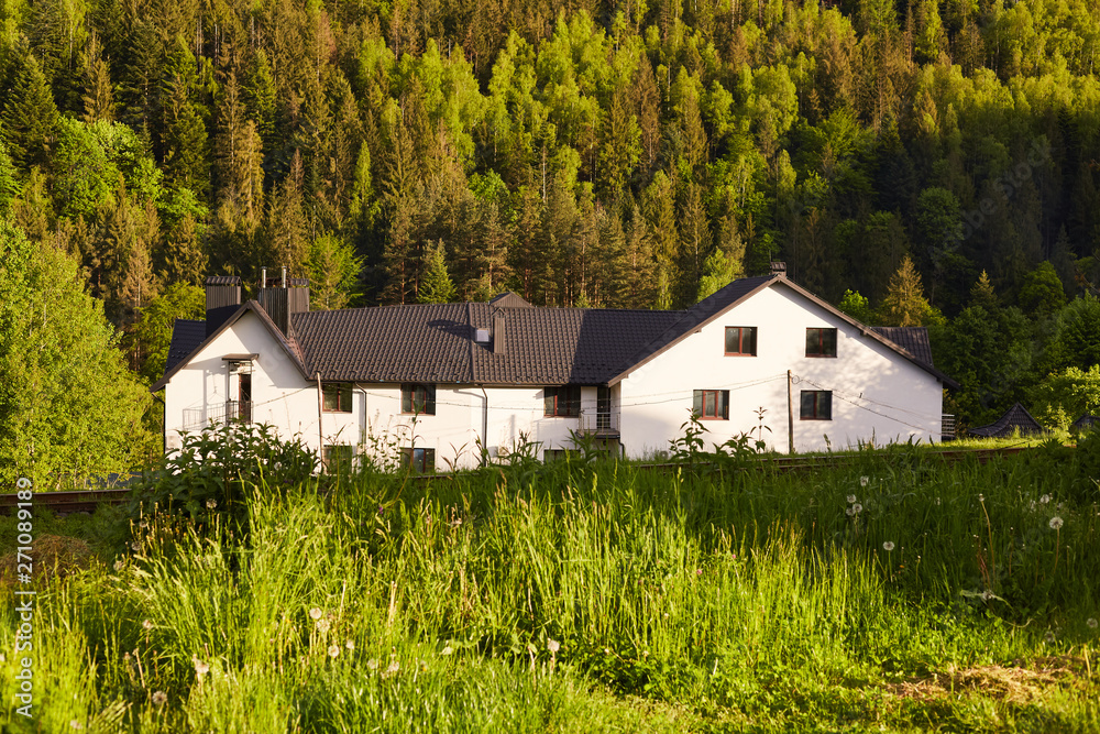 Obraz premium Shot of large white house in bottom of mountains, house situated near forest, guest house in mountains area, place for having rest with friends and family, beautiful landscape. Traveling concept.