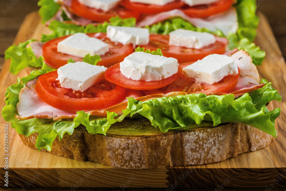 Delicious sandwich and lager beer on wooden table with dark background.