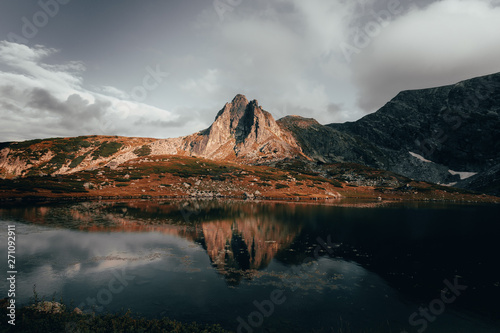 Mountain peak with reflection in water of a lake  cloudy sky and grass