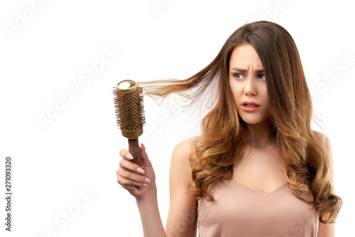 beautiful young girl combing her locks, and with a disgruntled, disappointed look on face looking intently at hairbrush. the concept of hair care and hair health.