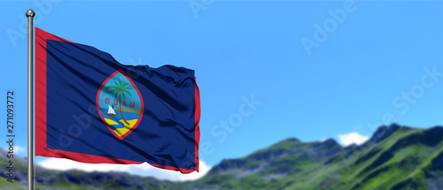 Guam flag waving in the blue sky with green fields at mountain peak background. Nature theme.