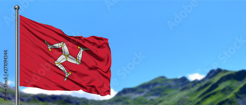 Isle Of Man flag waving in the blue sky with green fields at mountain peak background. Nature theme.