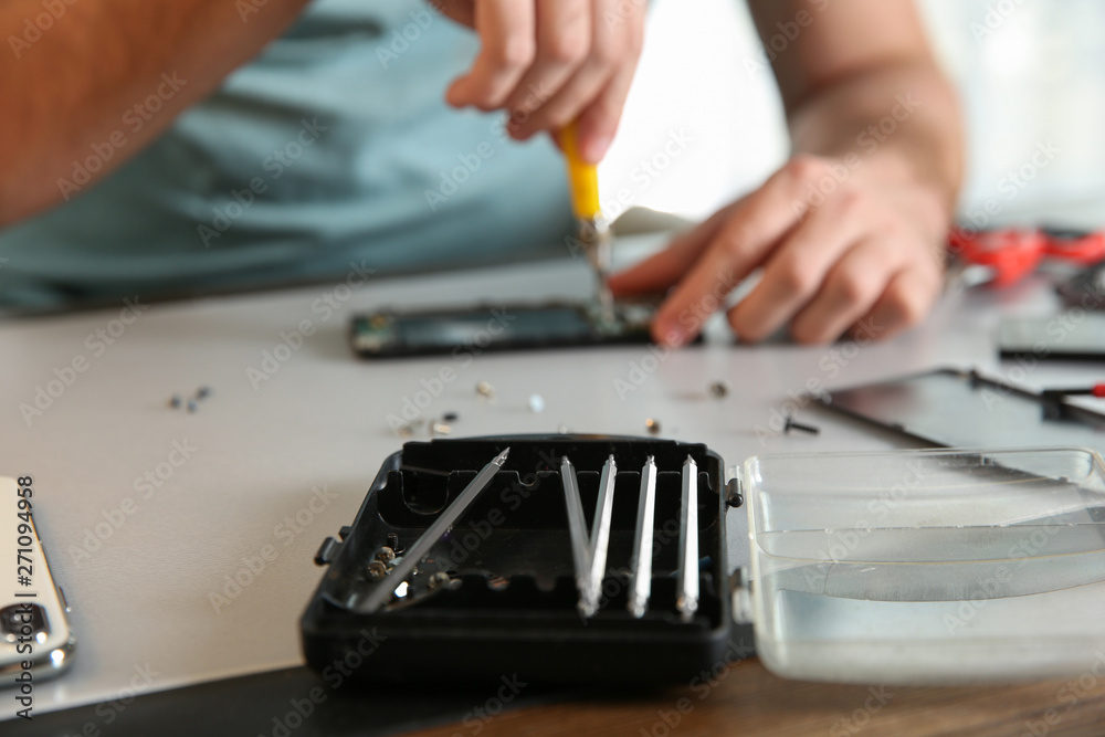 Toolbox in focus and blurred technician repairing mobile phone at table, closeup with space for text Toolbox in focus and blurred technician repairing mobile phone at table, closeup with space for text