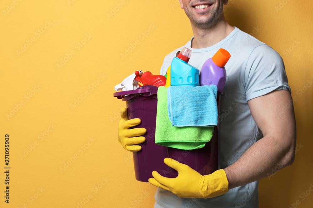 Man with bucket of detergents on color background, closeup. Space for text Man with bucket of detergents on color background, closeup. Space for text