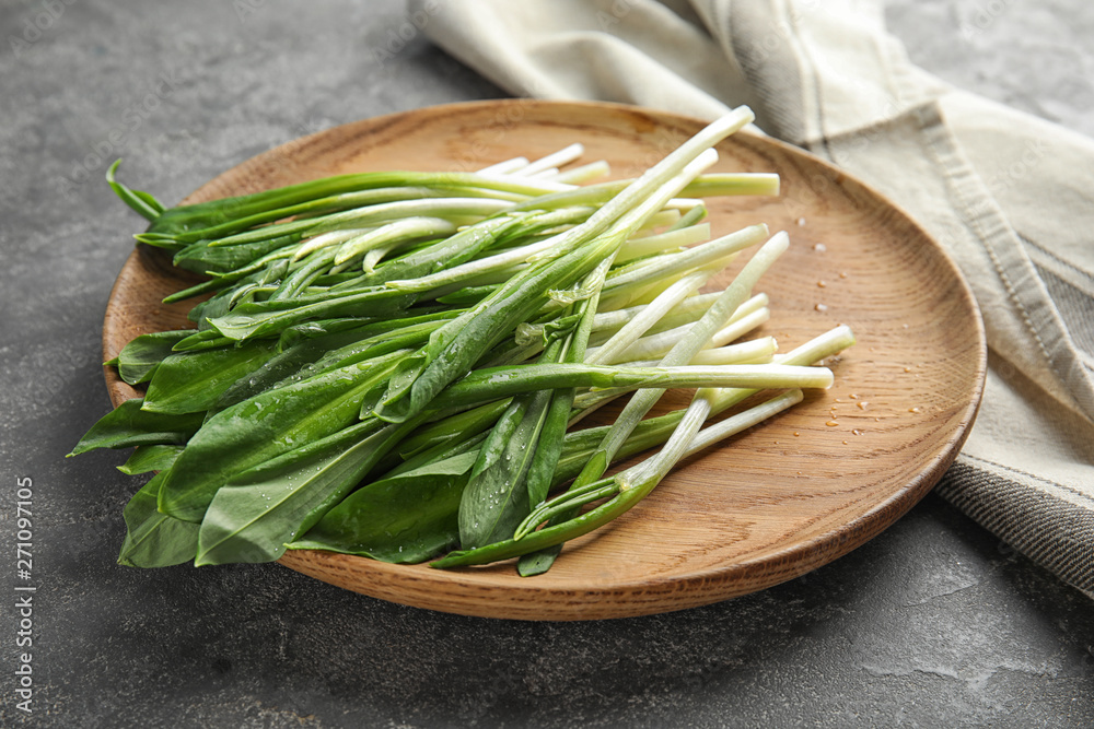 Wooden plate with wild garlic or ramson on grey table Wooden plate with wild garlic or ramson on grey table