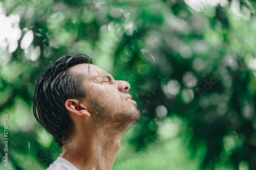 portrait young Asian man in raising head up and looking at sky during the rain