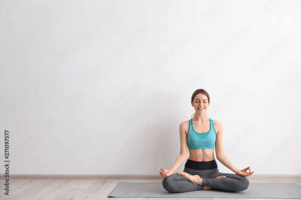 Young woman meditating near light wall, space for text. Zen concept Young woman meditating near light wall, space for text. Zen concept