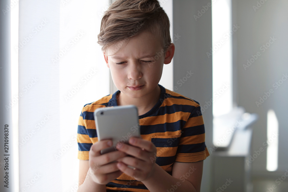 Sad little child with smartphone indoors. Danger of internet Sad little child with smartphone indoors. Danger of internet