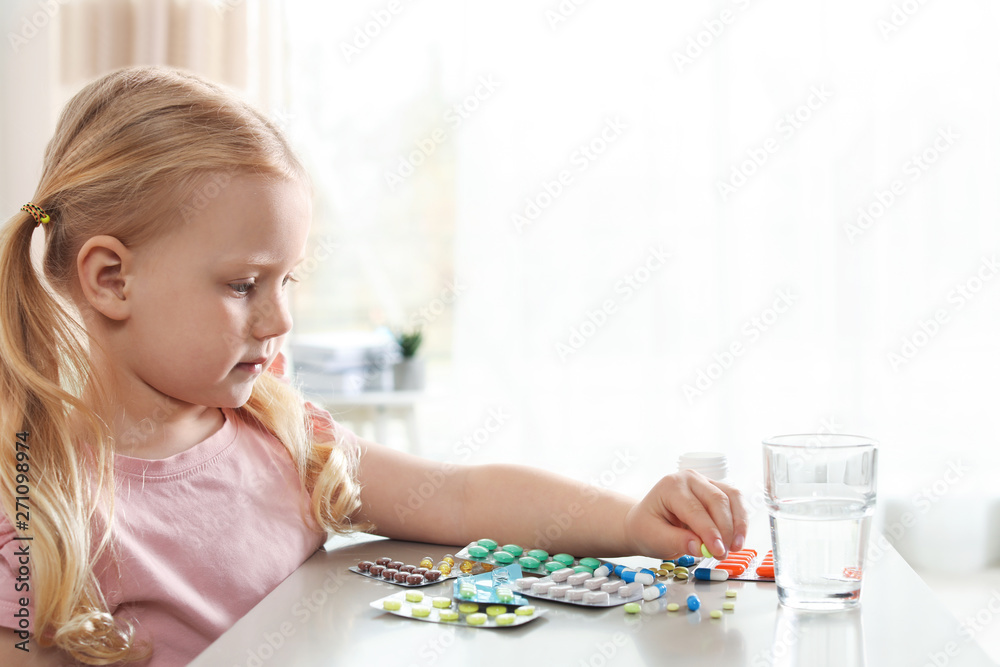 Little child with many different pills at table indoors. Danger of medicament intoxication Little child with many different pills at table indoors. Danger of medicament intoxication