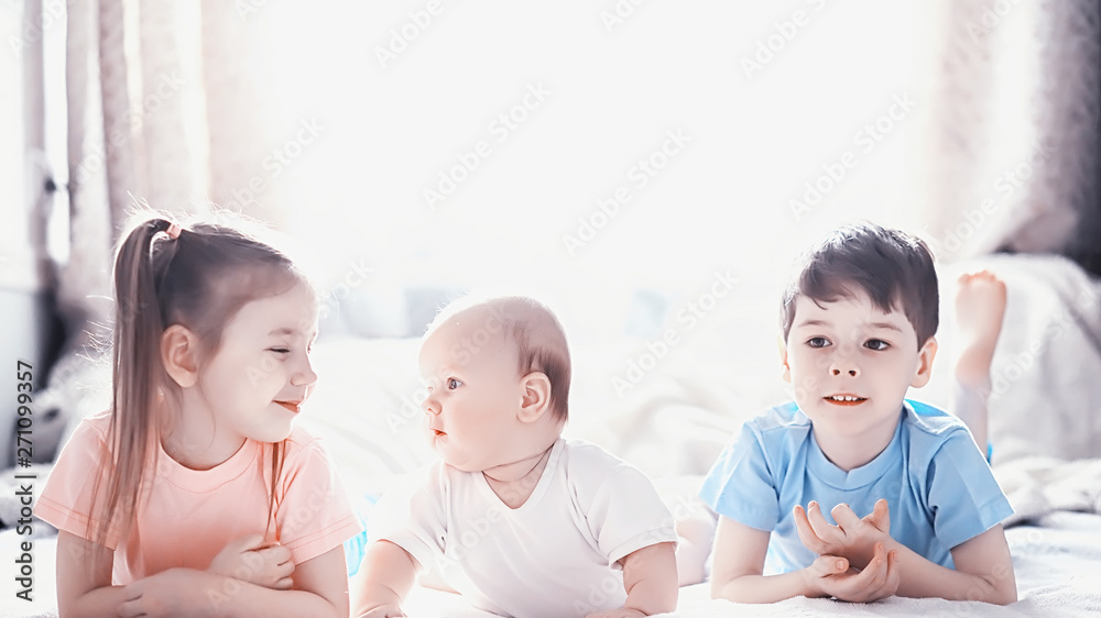 Children lie on the bed next to the newborn baby, little sister. Children lie on the bed next to the newborn baby, little sister.