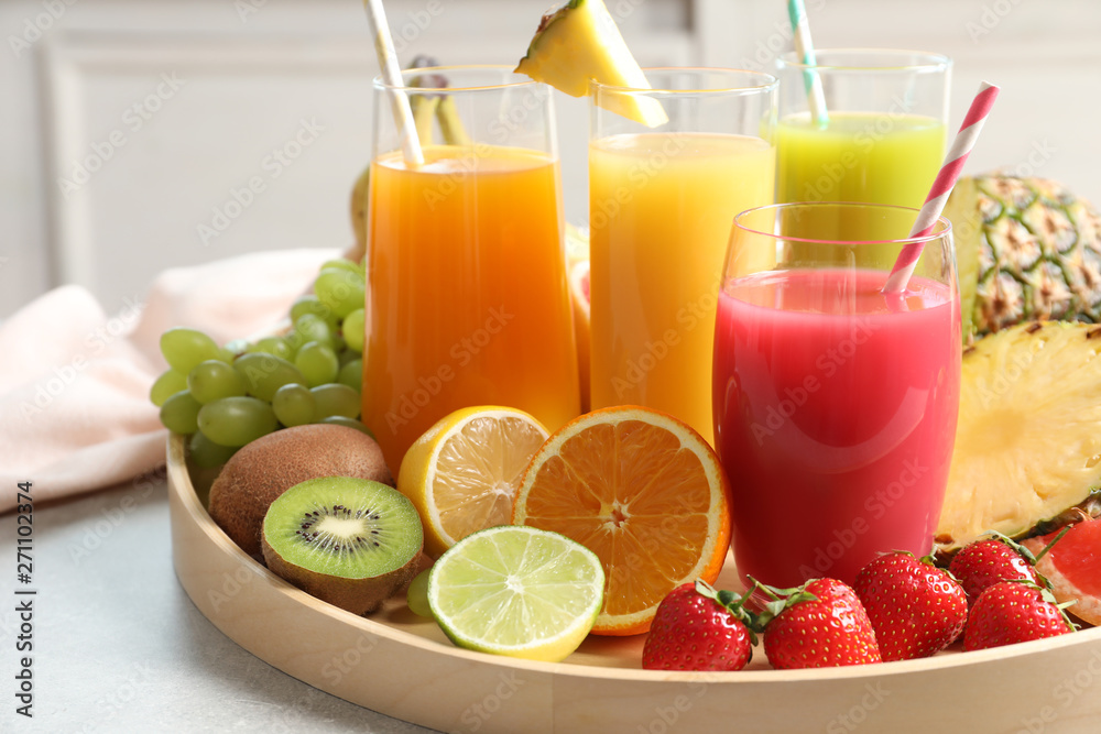 Fototapeta premium Wooden tray with glasses of different juices and fresh fruits on table
