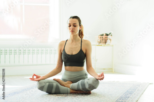 Young attractive smiling woman practicing yoga in a bright room