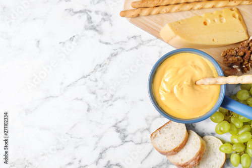 Flat lay composition with pot of delicious cheese fondue on marble table, space for text