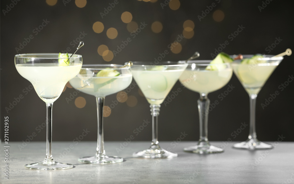 Glasses of martini with cucumber on grey table against blurred lights Glasses of martini with cucumber on grey table against blurred lights