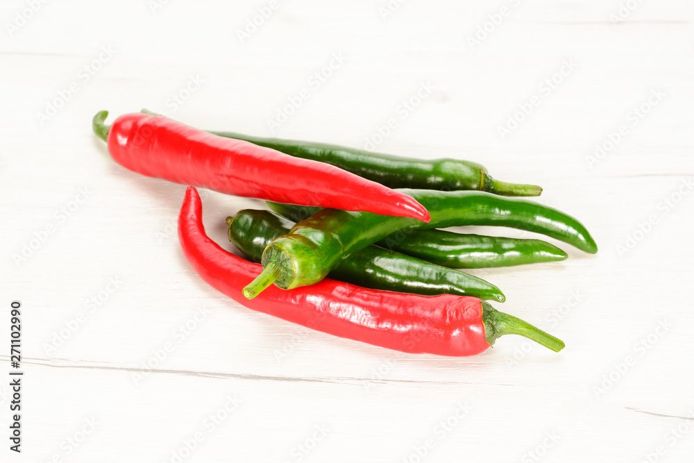 Red and green fresh chilli peppers on a white wooden table.