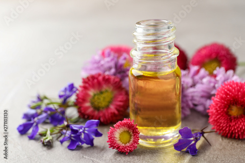 Bottle of essential oil with flowers on table. Space for text