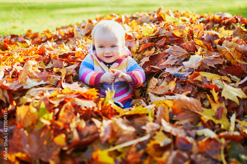 girl sitting in large heap of colorful autumn leaves on a fall day in park