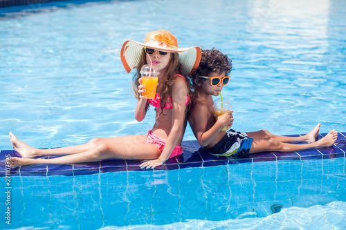 Two kids girl and boy drink juice in the pool and have fun. Children and summer concept