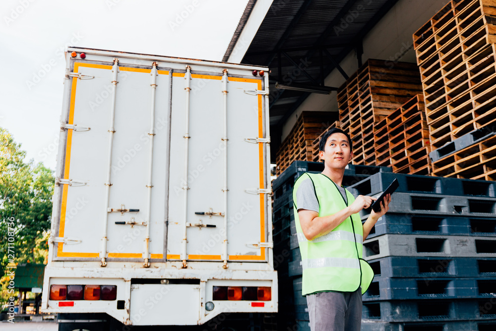 © twinsterphoto - Young Asian male logistics warehouse distribution business entrepreneur wearing reflective jacket using a digital tablet. He is surrounded by plenty of pallets and truck in shipping cargo. © twinsterphoto - Young Asian male logistics warehouse distribution business entrepreneur wearing reflective jacket using a digital tablet. He is surrounded by plenty of pallets and truck in shipping cargo.