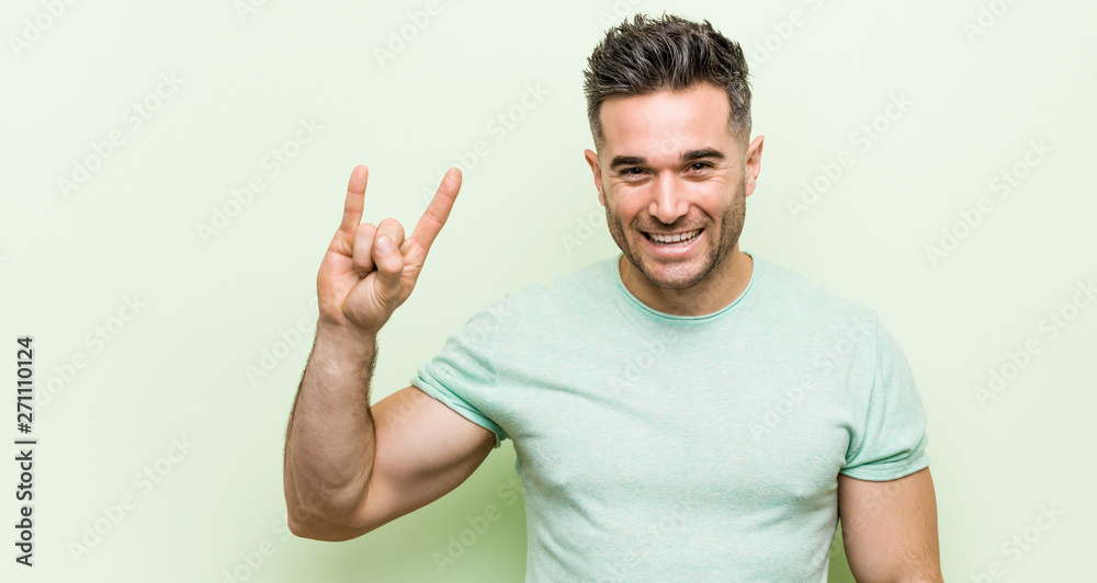 Young handsome man against a green background showing a horns gesture as a revolution concept. Young handsome man against a green background showing a horns gesture as a revolution concept.
