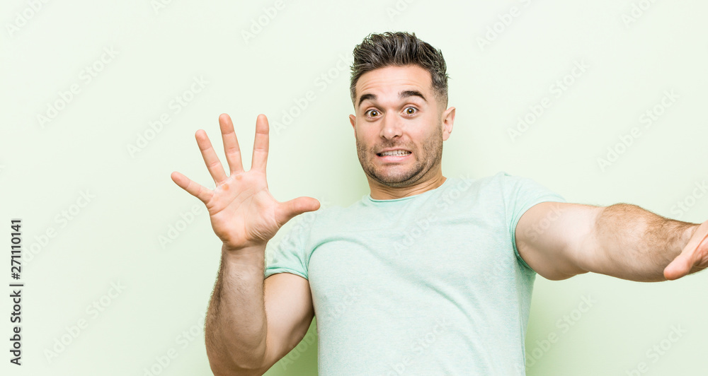 Young handsome man against a green background being shocked due to an imminent danger Young handsome man against a green background being shocked due to an imminent danger