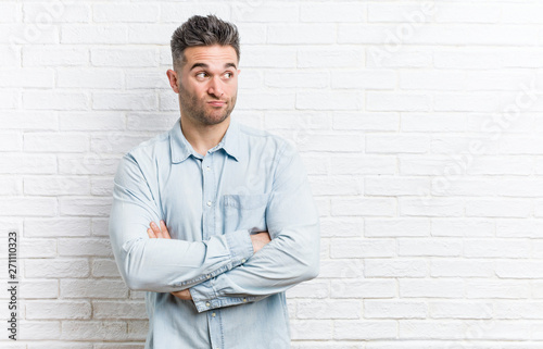 Young handsome man against a bricks wall unhappy looking in camera with sarcastic expression.