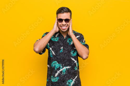 Young filipino man wearing summer clothes covering ears with hands.