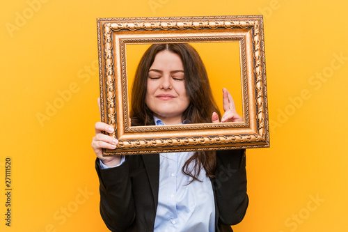 Young curvy plus size business woman holding a frame crossing fingers for having luck © Asier
