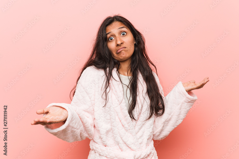 Young indian woman wearing pajama doubting between two options.