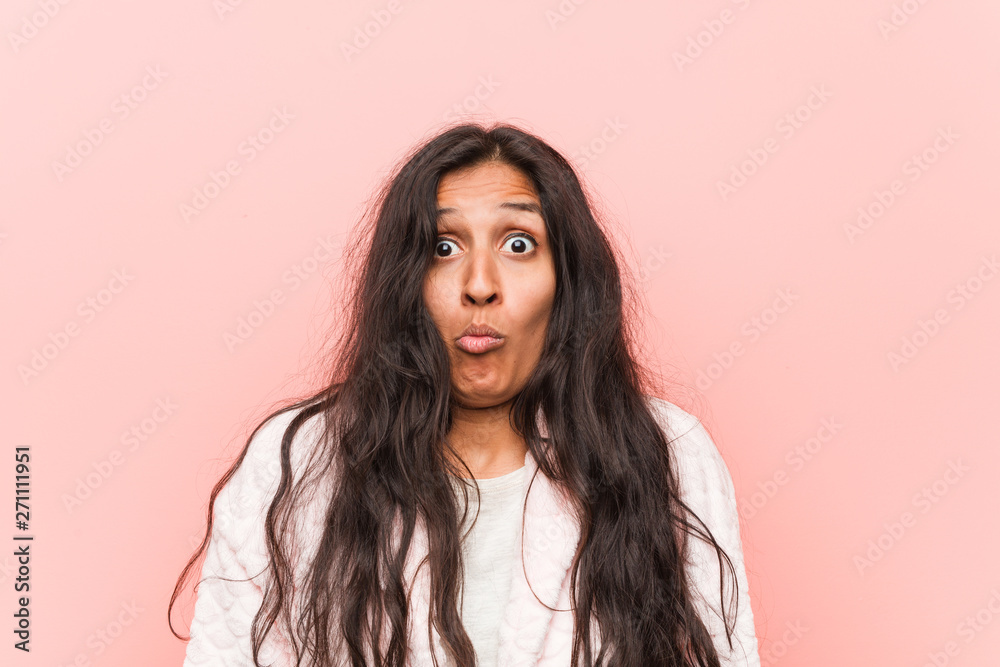 Young indian woman wearing pajama shrugs shoulders and open eyes confused.