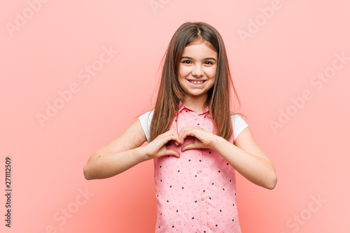 Cute little girl smiling and showing a heart shape with him hands.