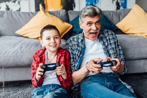 Active inspired man and his grandson enjoying new video game.. Sit on floor in living room.