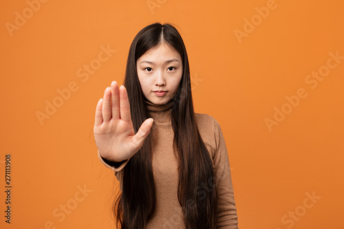 Young pretty chinese woman standing with outstretched hand showing stop sign, preventing you. photo