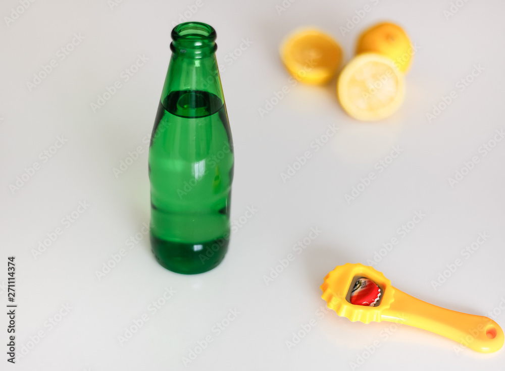 Green glass bottle of fizzy drink and bottle opener on the white background. Drinking mineral water. Green glass bottle of fizzy drink and bottle opener on the white background. Drinking mineral water.
