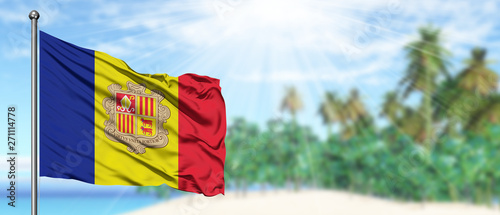 Waving Andorra flag in the sunny blue sky with summer beach background. Vacation theme, holiday concept.