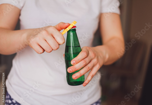 Woman in a light color t-shirt opens a green bottle of fizzy drink with a yellow opener