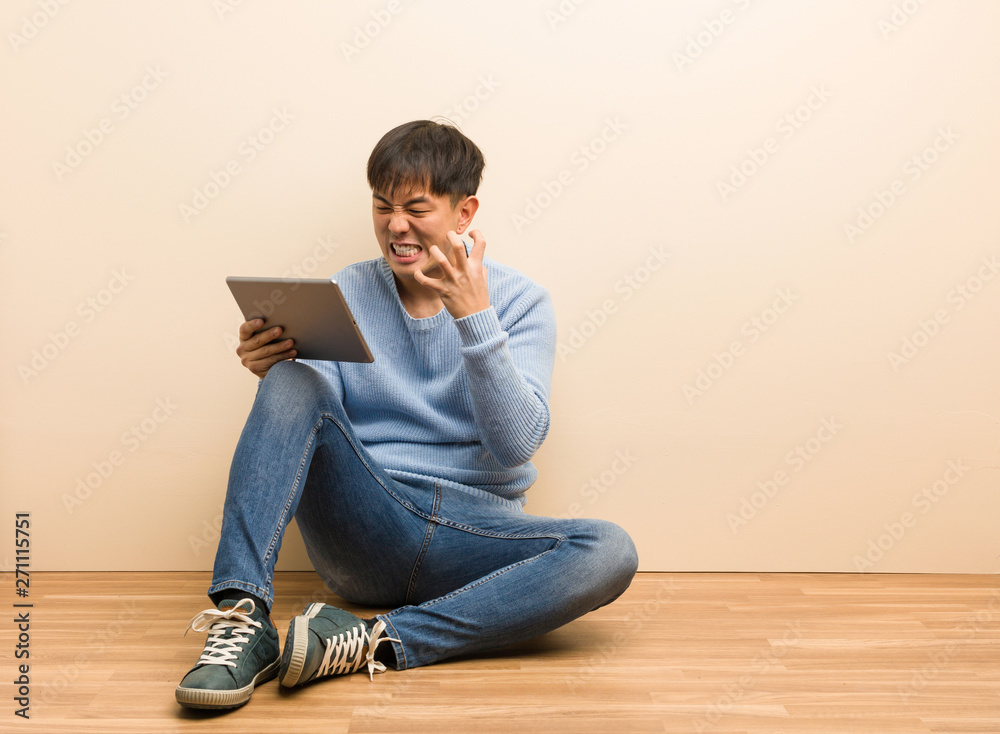 Young chinese man sitting using his tablet angry and upset